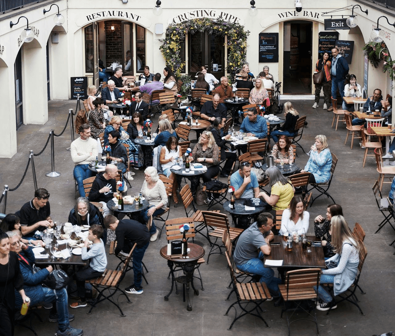Courtyard filled with numerous people dining outdoors at tables under string lights.