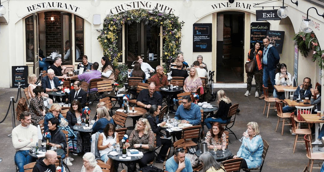 A lively outdoor courtyard filled with patrons dining and socializing at restaurants and bars.